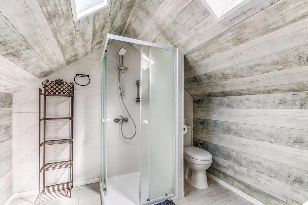 Une salle de bain avec une douche à parois de verre, des toilettes et une étagère en métal.