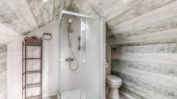 A bathroom with a glass-enclosed shower, a toilet, and a metal shelf.