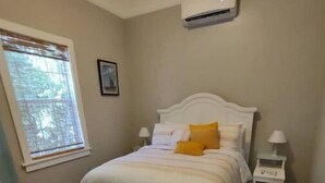 A bedroom with a bed, a nightstand, an air conditioning unit, and a window with blinds. - 2feather inn #2 (Natchez)