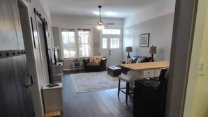 A spacious living area with a sofa, a coffee table, and a dining table. There is a kitchen area with a refrigerator and a microwave. The room has a ceiling fan and a window providing natural light. - 2feather inn #2 (Natchez)