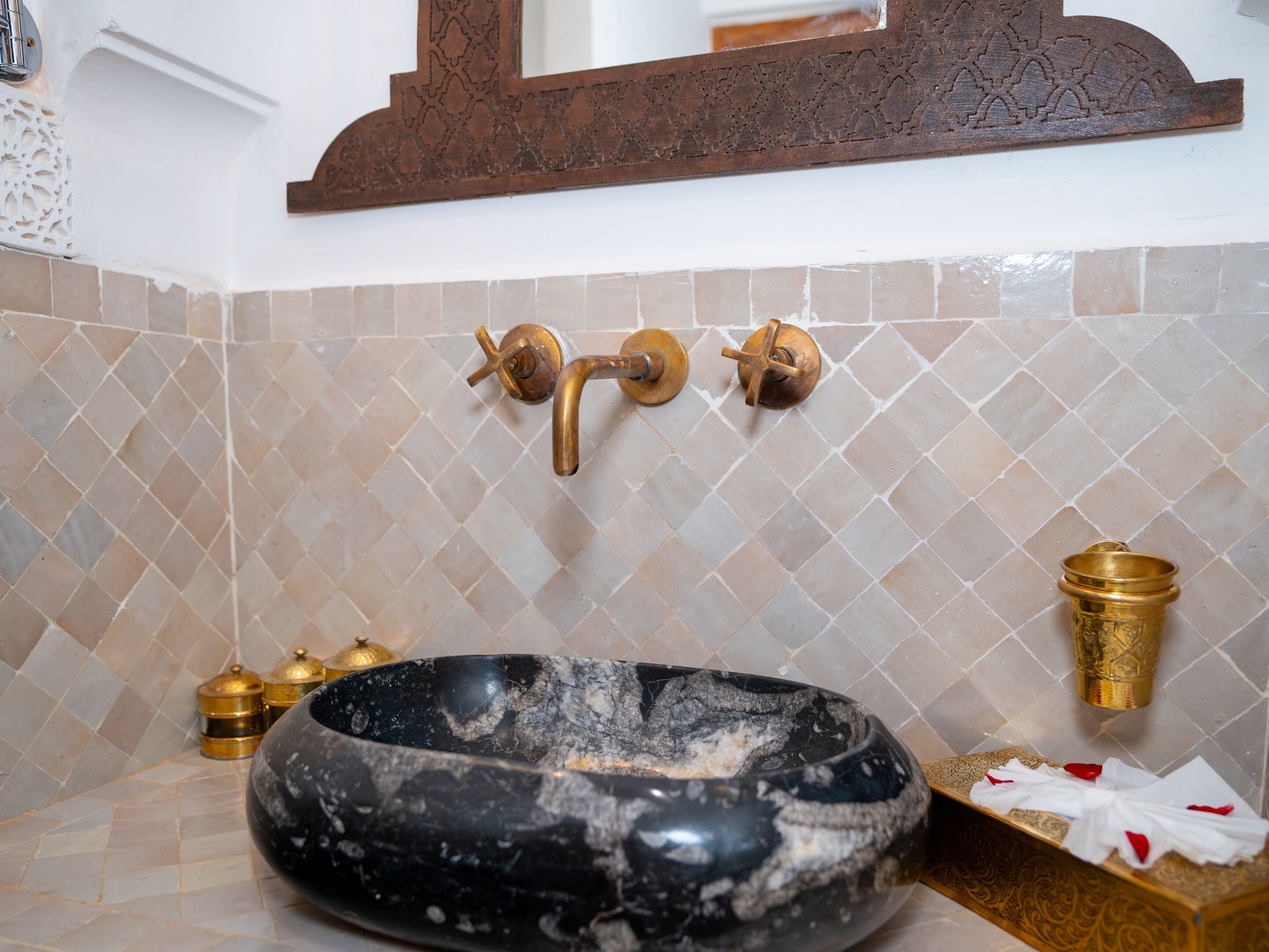 A bathroom with a black marble sink, gold fixtures, and patterned tiles.