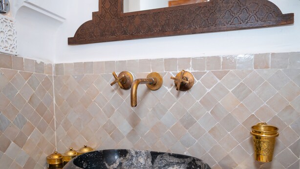 Un baño con lavamanos de mármol negro, grifería dorada y azulejos con diseño.