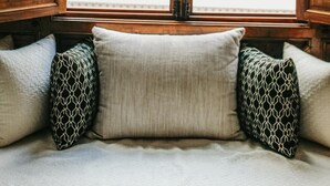A window with intricate wooden carvings, a cushioned bench with patterned pillows, and a view of a building with white balconies. - Riad Nelia (Marrakech)