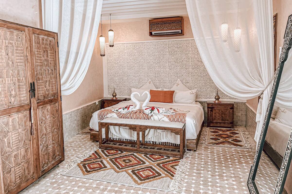 A bedroom with a bed, a wooden wardrobe, a patterned rug, and a decorative mirror.