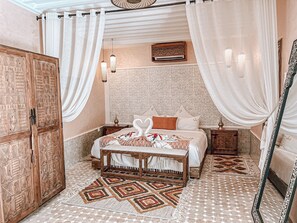 A bedroom with a bed, a wooden wardrobe, a patterned rug, and a decorative mirror.