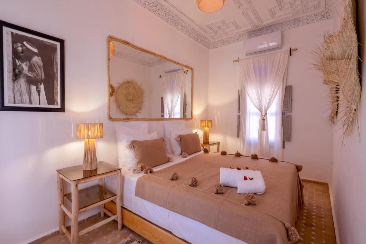 A bedroom with a large bed, two bedside tables, a mirror, and a framed picture on the wall.