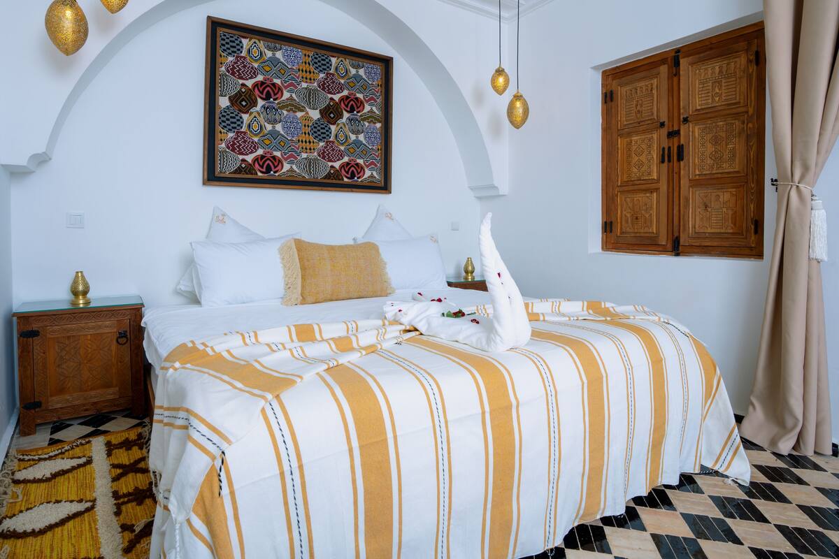 A hotel room with a bed, a nightstand, a decorative wall piece, and a wooden wardrobe.