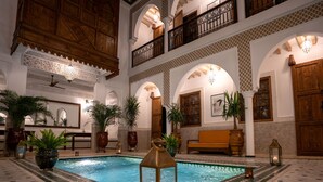Una piscina interior con una linterna, rodeada de plantas en macetas y mobiliario de madera.