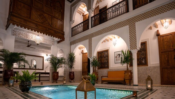 An indoor swimming pool with a lantern, surrounded by potted plants and wooden furniture. - Riad Nelia (Marrakech)