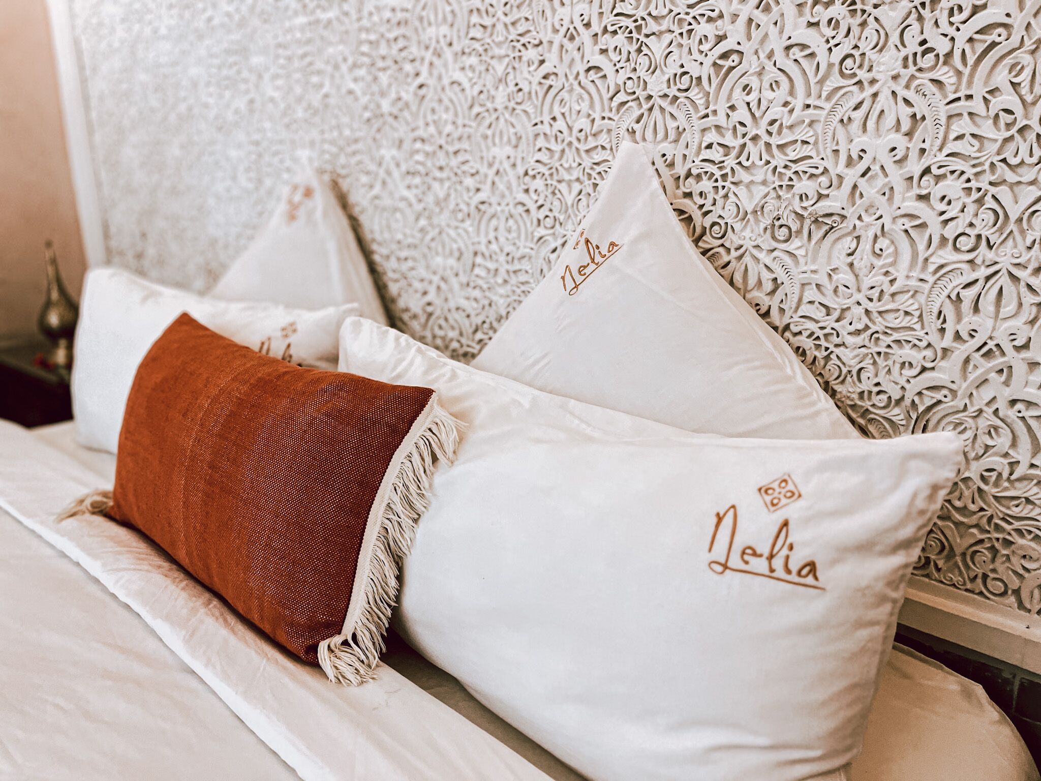 A neatly made bed with white and brown pillows, one of which has "Nola" embroidered on it.