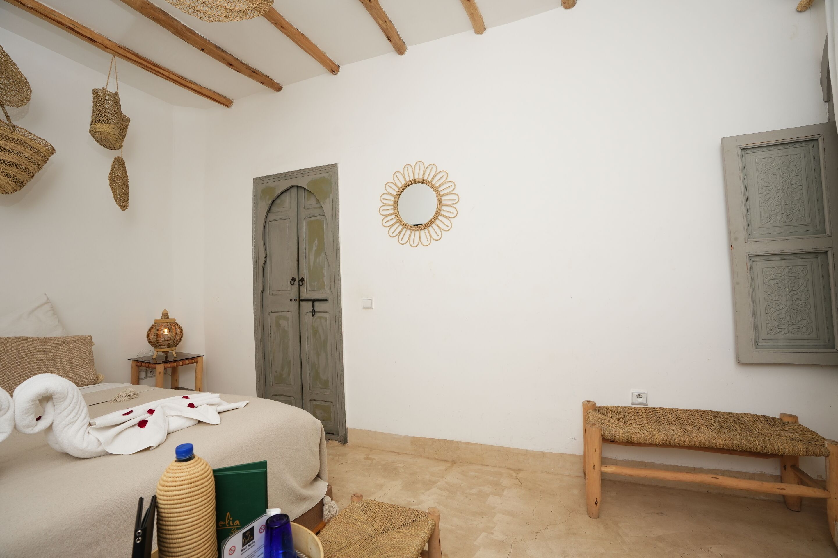 A bedroom with a bed, a wooden bench, a woven basket, a mirror, and a door.