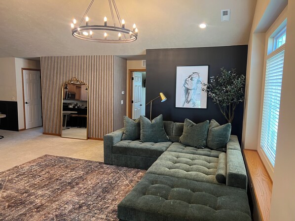 A modern living room with a sectional sofa, a patterned rug, a chandelier, and a framed artwork on the wall. - Luxe+Elegance Sleeps 6 2bedrooms 2bath (Lincoln)