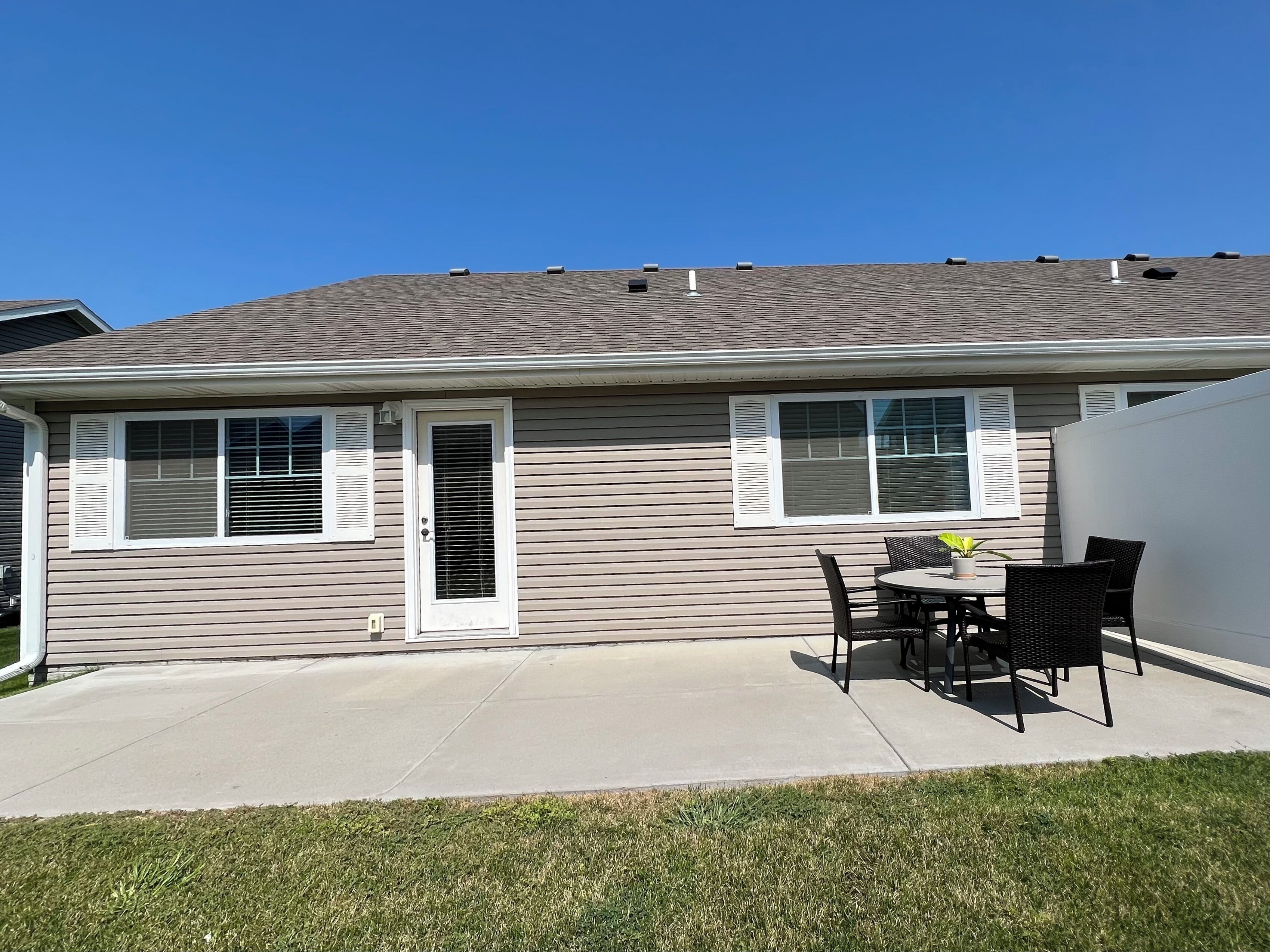 A residential house with a patio, a sliding glass door, and a small outdoor seating area with a table and chairs.