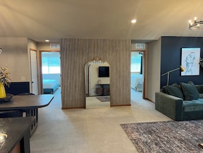 A modern living room with a sofa, a coffee table, and a TV. There is a striped partition and a door leading to another room. - Luxe+Elegance Sleeps 6 2bedrooms 2bath (Lincoln)