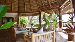 Un espace extérieur abrité, doté de mobilier en bois, de plantes en pot et d’un toit de chaume.
