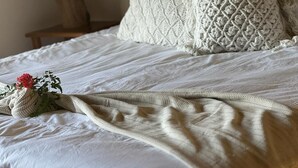 Un lit bien fait, avec une couette blanche et une couverture tricotée.