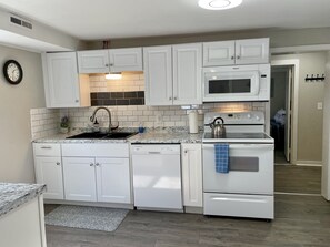 Una cocina moderna con armarios blancos, un microondas integrado, un horno y un lavavajillas.