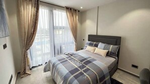 Un dormitorio moderno con una cama grande, cabecera y vistas al exterior a través de cortinas translúcidas.