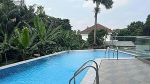 Una piscina con barandillas metálicas, rodeada de exuberante follaje y una casa al fondo.