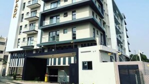 Un edificio de varios pisos con diseño moderno, que cuenta con balcones y un estacionamiento.
