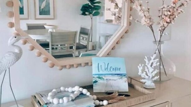 Un mobile toilette con uno specchio decorativo, un cartello di benvenuto e un vassoio con oggetti decorativi.