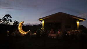 A building with a crescent moon decoration in front, a covered outdoor seating area, and a well-lit entrance. - Villa Luna del Arenal (La Fortuna)