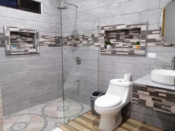 Un baño con ducha de vidrio, inodoro, lavamanos y azulejos decorativos.