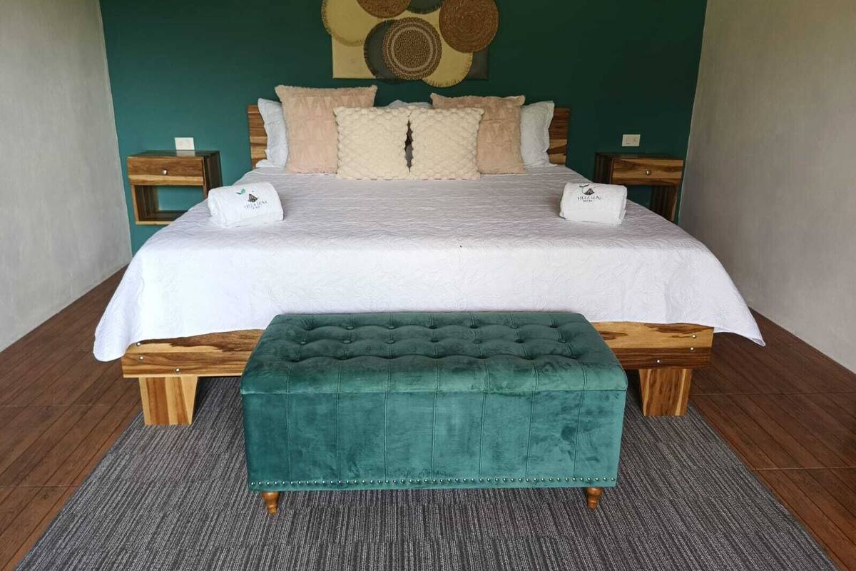 A neatly made bed with a white duvet, two pillows, and two matching towels. In front of the bed is a green upholstered bench.