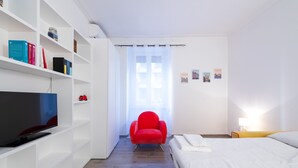 A modern hotel room with a TV, a red armchair, a bed, and a window with a curtain. - Casa Riboty - One Bedroom Apartment, Sleeps 2 (Rome)