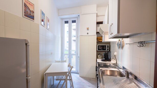 A narrow kitchen with white cabinets, a stainless steel sink, and a white refrigerator. There is a small table with a chair in the center. - Casa Riboty - One Bedroom Apartment, Sleeps 2 (Rome)