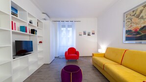 A modern living room with a flat-screen TV, a red armchair, a yellow sofa, and a purple ottoman. - Casa Riboty - One Bedroom Apartment, Sleeps 2 (Rome)