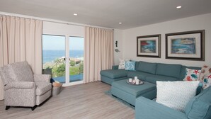 Una sala de estar con vista al océano, un sofá, una silla y dos cuadros en la pared.