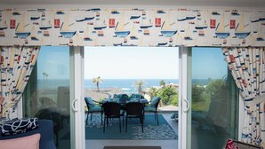Habitación con puerta de vidrio corrediza que da a un patio con mesa y sillas, un sofá y vista al océano.