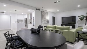 A modern living room with a round dining table, a green sofa, and a flat-screen TV. - CBD International Apartments (Wagga Wagga)