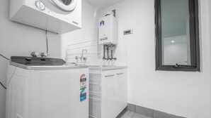 A laundry room with a front-loading washer, a stacked dryer, and a water heater. - CBD International Apartments (Wagga Wagga)