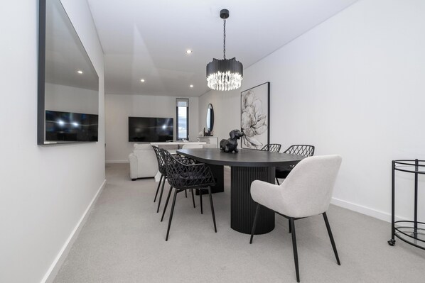 A modern dining area with a round table, black and white chairs, a chandelier, and a large mirror on the wall.