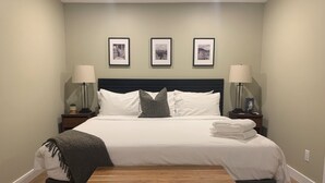 A neatly made bed with white linens and pillows, flanked by two bedside tables with lamps, in a room with a dark headboard and light walls. - Oliver Oasis, Merlot - Vineyard home with great pool, hot tub & views for days!  (Osoyoos)