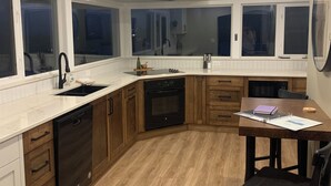 A modern kitchen with wooden cabinets, a built-in oven, and a dining table with chairs. - Oliver Oasis, Merlot - Vineyard home with great pool, hot tub & views for days!  (Osoyoos)