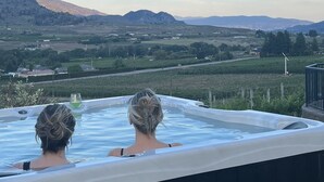 Two people in a hot tub overlooking a scenic landscape with mountains and vineyards. - Oliver Oasis, Merlot - Vineyard home with great pool, hot tub & views for days!  (Osoyoos)