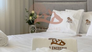 Una cama bien hecha con sábanas y almohadas blancas, un jarrón decorativo con flores y un cabecero con el logo de un árbol.