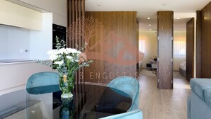 Un salón moderno con una mesa de centro de vidrio, dos sillones azules y un jarrón decorativo con flores.