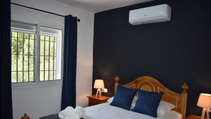 A neatly made bed with white linens, blue pillows, and a wooden headboard. There are two bedside tables with lamps, and a window with curtains.