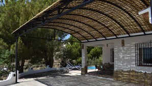 A covered outdoor area with a pool, lounge chairs, and a dining table.