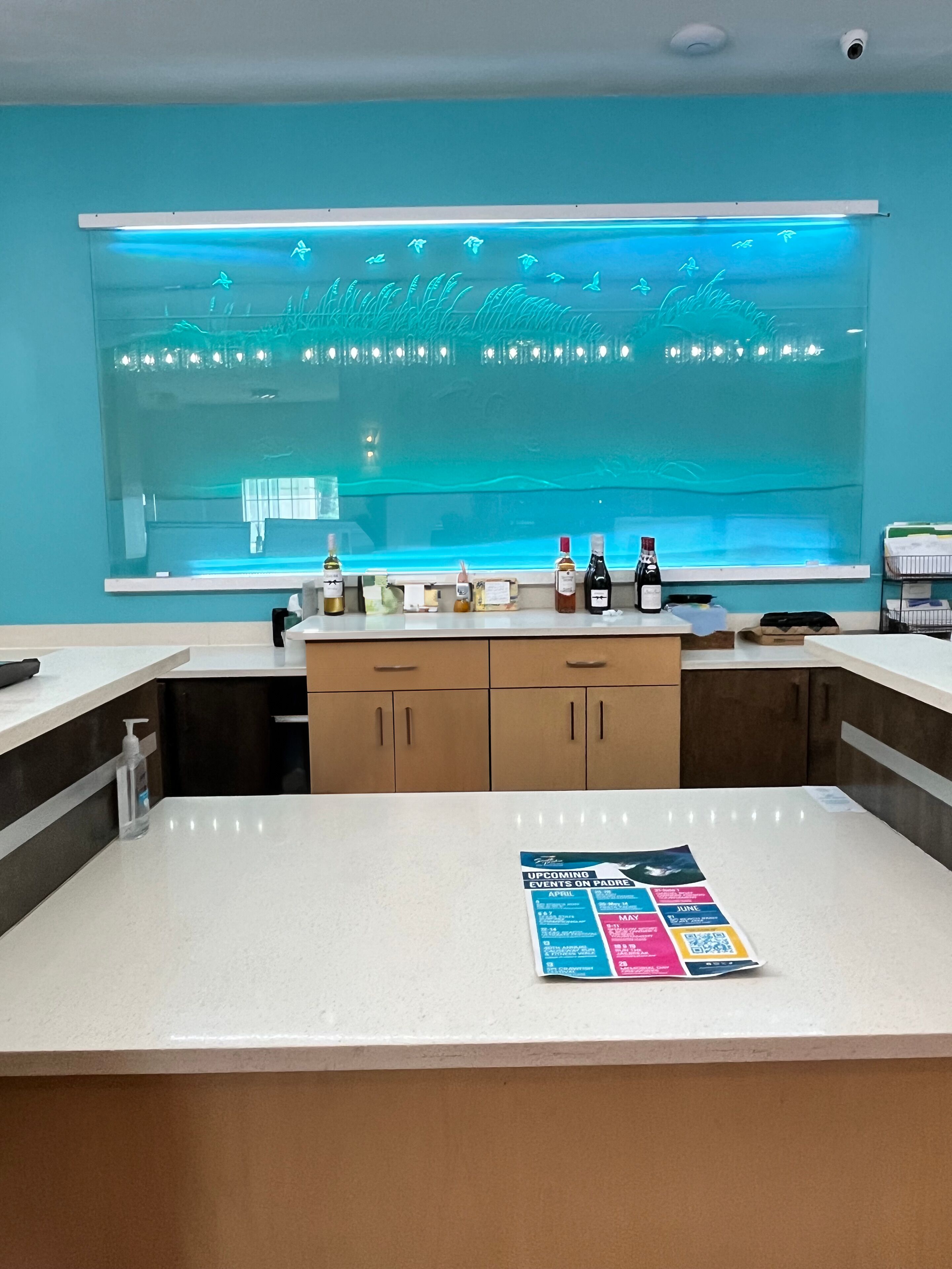 Eine Bar mit einem großen, beleuchteten Aquarium, einer Theke mit Flaschen und einem Plakat, das kommende Veranstaltungen bewirbt.
