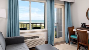 A room with a view of the beach, a dining area with chairs, a table, and a coffee maker.