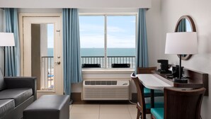 A hotel room with a balcony, a sofa, a table with a lamp, a chair, and a coffee maker.