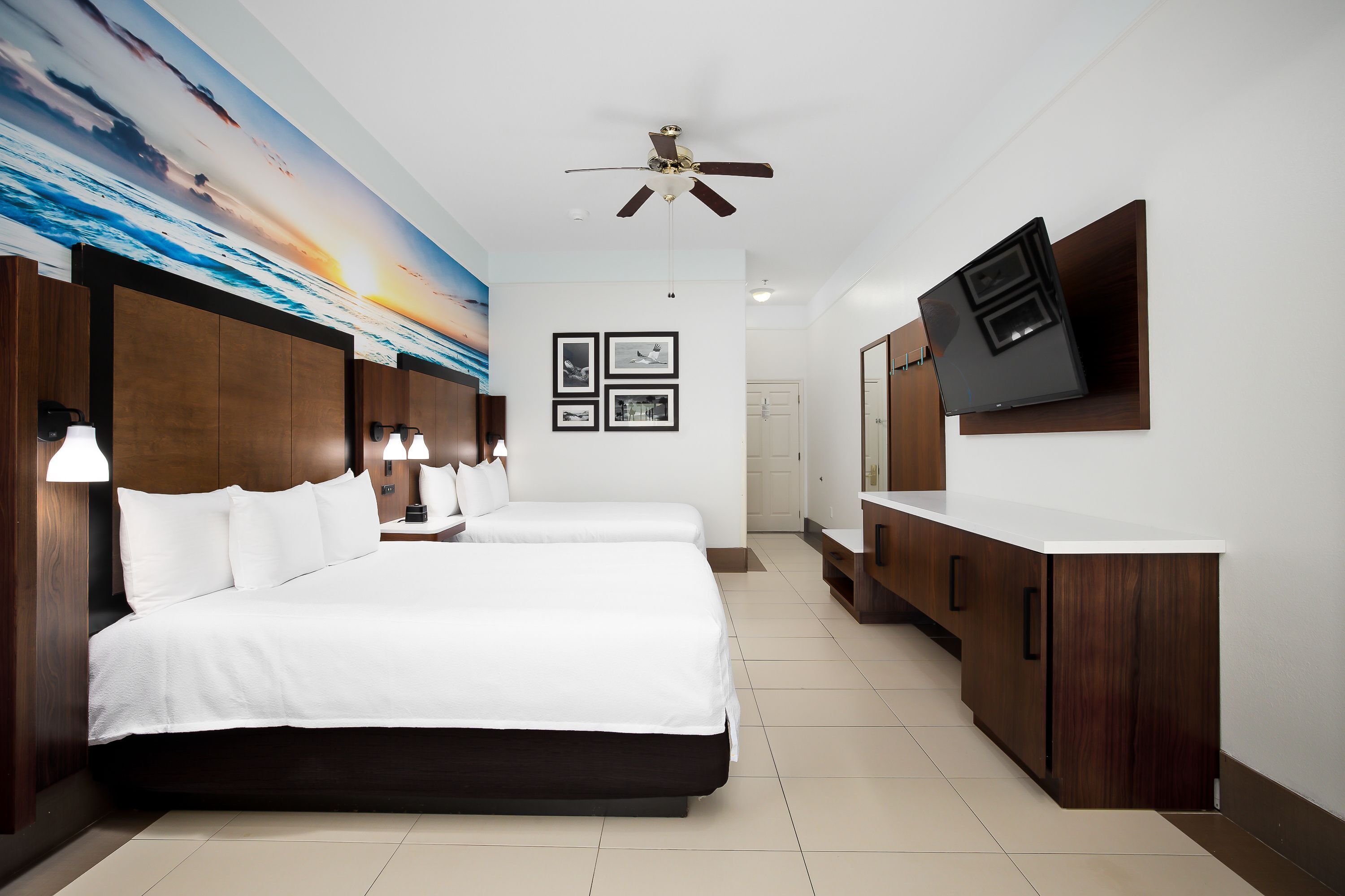 Quarto de hotel com uma cama grande, uma escrivaninha, uma televisão e um ventilador de teto.