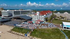 A hotel with multiple buildings, a swimming pool, and a beach area with umbrellas and lounge chairs.