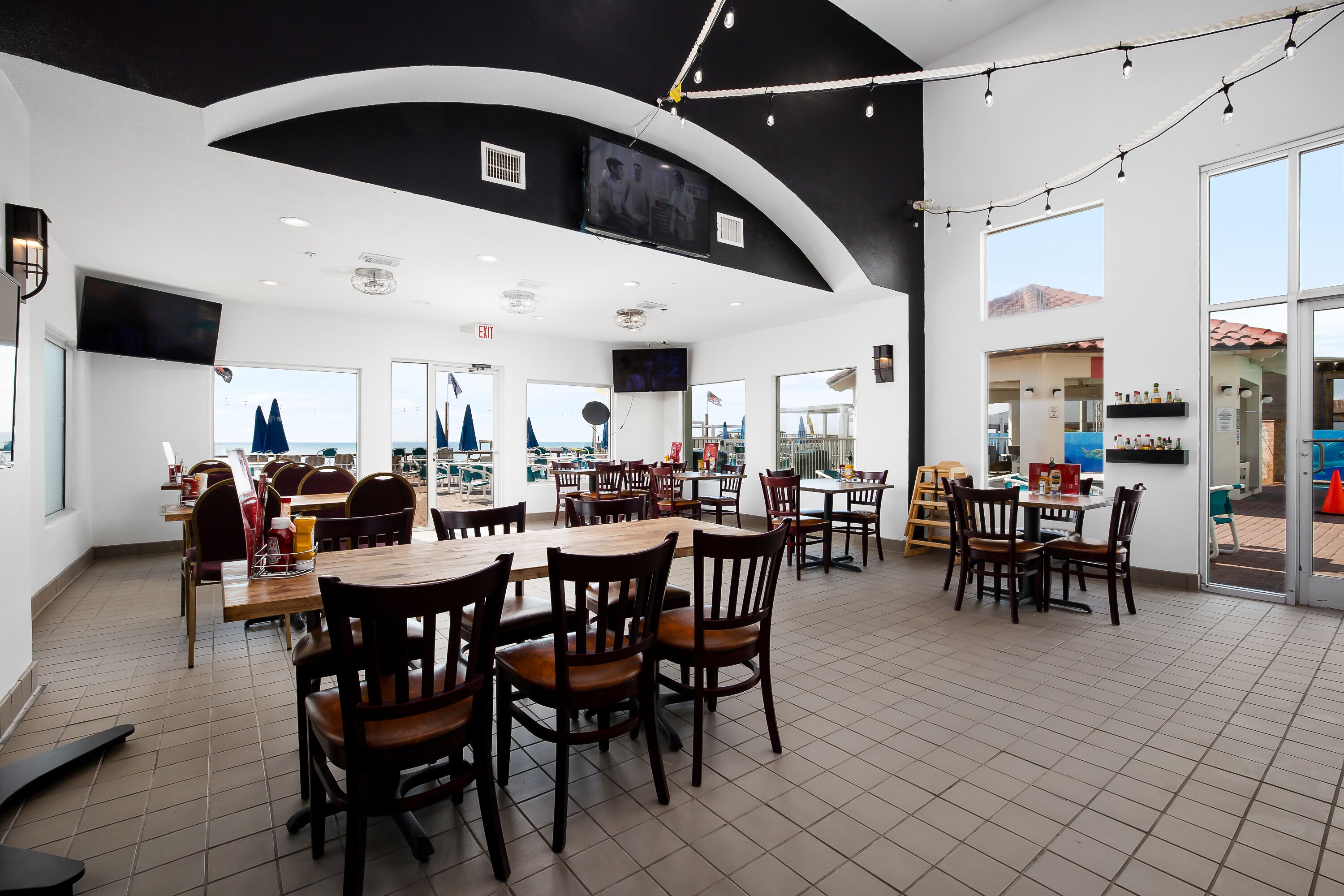 A spacious restaurant with multiple tables and chairs, large windows offering views of the sea, and a modern interior design.