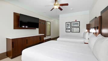 Habitació d'hotel amb un llit gran, un televisor fixat a la paret, un ventilador de sostre i una taula de nit amb làmpades.